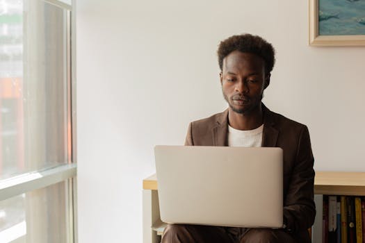 An adult professional male working on a laptop in a bright, modern office setting.