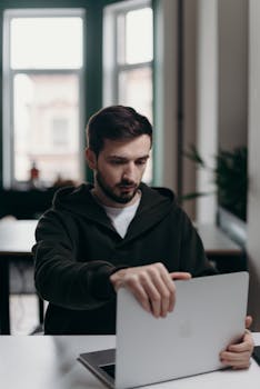 Focused young man using a laptop, working in a modern home office setting.