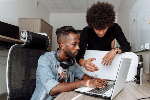 Two diverse male colleagues collaborating on a laptop in a modern office environment.
